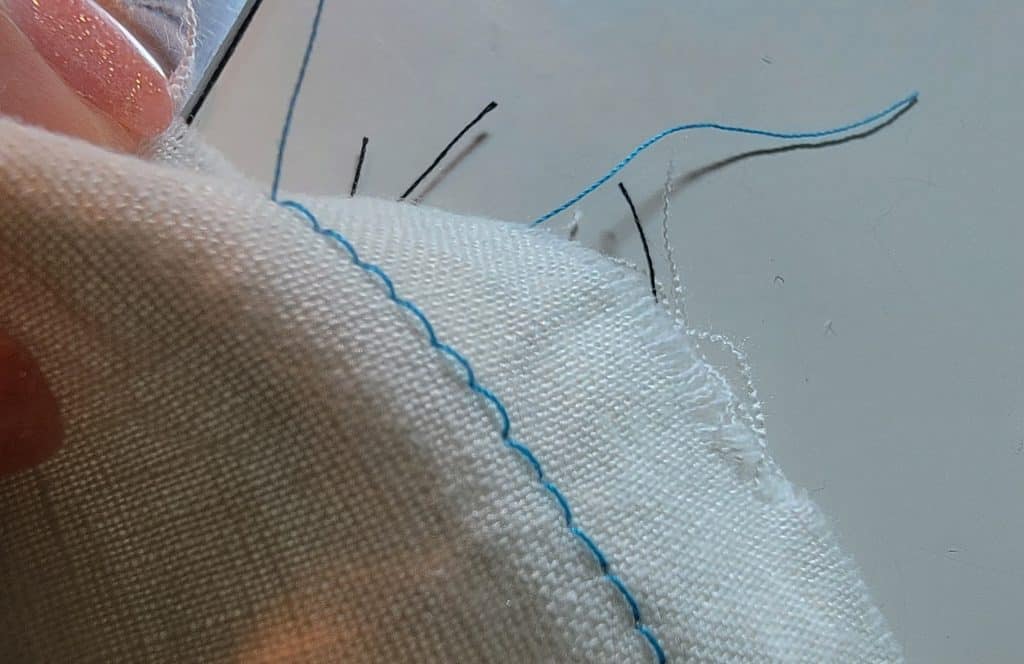Blue loose sewing machine stitches on white fabric. Stitches are baggy and hang away from fabric.