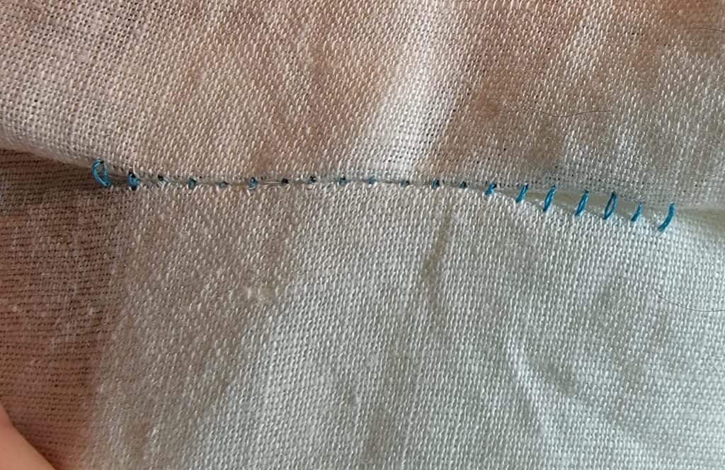 Blue loose sewing machine stitches on white fabric. Fabric pulls apart easily and reveals the blue stitches.