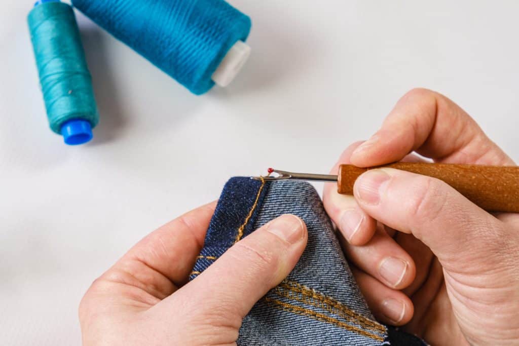 Using a seam ripper to remove a hem on denim jeans. Blue thread in the background.